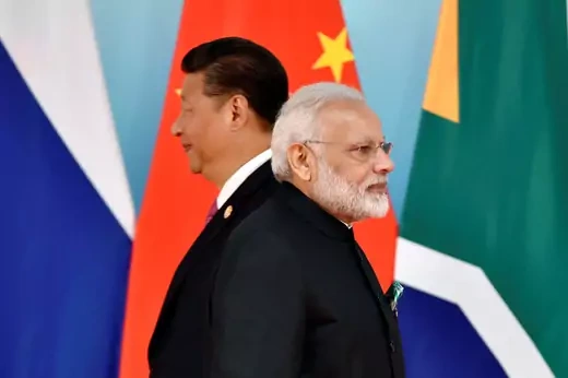 Prime Minister Modi of India and President Xi Jinping of China stand next to one another facing opposite directions, with national flags hanging in the background.