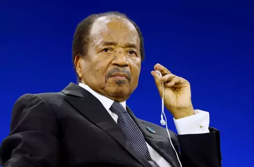 President of Cameroon, Paul Biya, sits while holding a pair of wire headphones in his hand.  