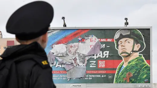 A military cadet stands in front of a billboard promoting contract army service in Saint Petersburg.