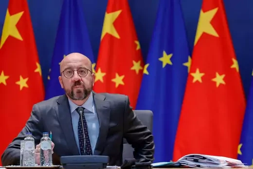 European Council president sits in a chair in front of the flags of the EU and China.