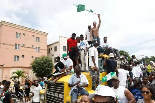 Supporters of Labour Party candidate Peter Obi surround and stand atop of a yellow truck. One man is pictured carrying the Nigerian flag. 