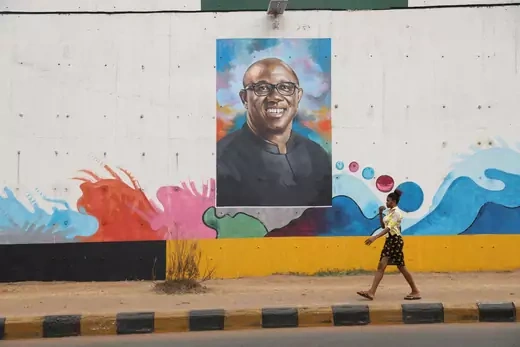 A woman walks by a wall filled with colorful graffiti with a large portrait of Labour Party (LP) Presidential candidate, Peter Obi.
