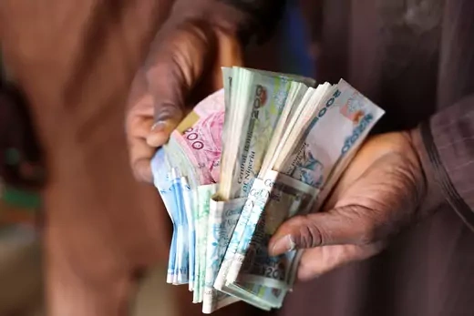 A man holds various stacks of Naira cash in his hands and counts the bills. 