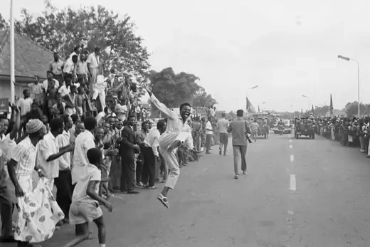 Man jumps of joy in front of crowd lining the street to celebrate Congo's independence.