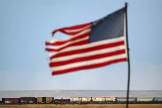 A torn U.S. flag waves above a moving freight train 