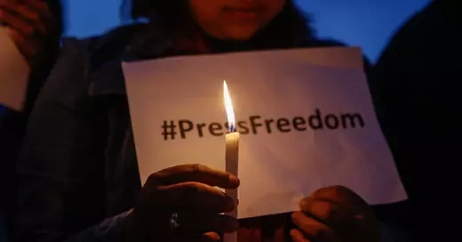 Person holds a candles in front of a sign that reads #PressFreedom.