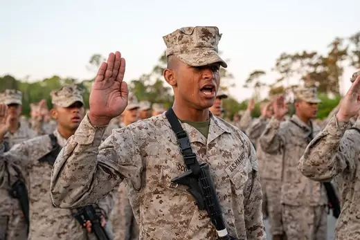 Soldier surrounded by fellow service members holds right hand up in pledge.
