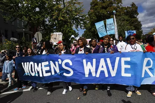 Women protest holding a blue sign reading "Women's Wave"