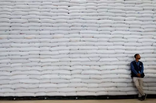 A worker in a blue jacket stands in front of stacked bags of wheat at an official visit to the World Food Program warehouse in Adama, Ethiopia. 