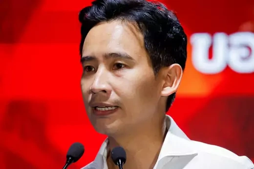 Thai Move Forward politician wears a white, button-down shirt while speaking into a microphone in front of a red background.