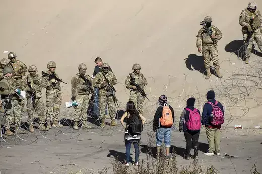 Migrants look across the southern U.S. border at National Guard troops.