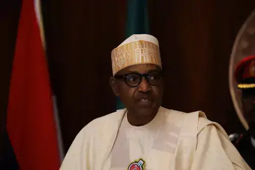 Nigerian President Muhammadu Buhari speaks while wearing white clothing and a traditional white hat.