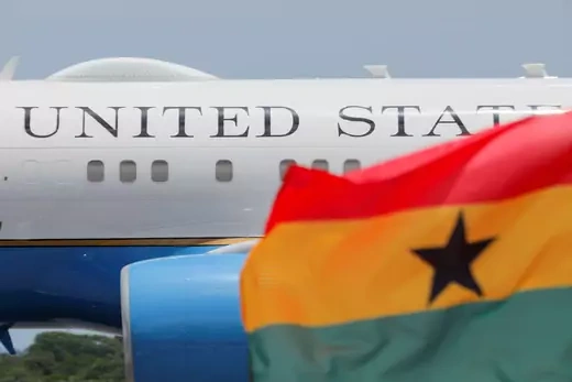 The flag of Ghana is shown waving in front of a United States government plane. 