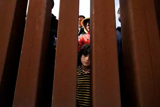 A migrant boy peers through the border wall near San Diego ahead of the end of Title 42 restrictions.