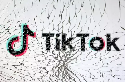 TikTok logo is seen through broken glass.