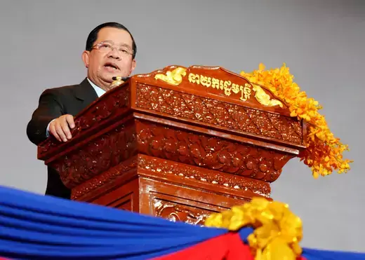 Cambodian Prime Minister Hun Sen speaks in front of an ornate wooden dais wearing a black suit.