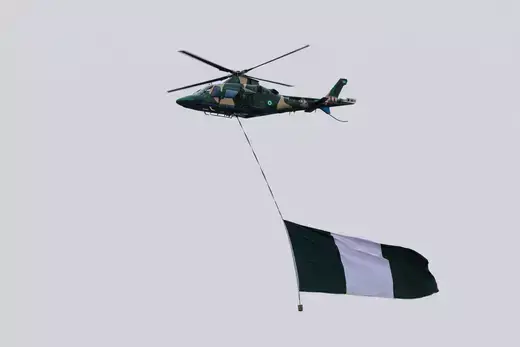 A Nigerian military helicopter is captured in the air with a Nigerian flag hanging from the bottom during the inauguration of Nigeria's President Bola Tinubu.