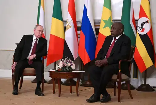 Russian President Vladimir Putin and South African President Cyril Ramaphosa sit together in front of a row of flags.