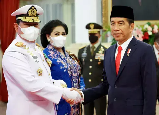 Commander of the Indonesian National Armed Forces wears a white military unifrom while shaking the hand of Indonesian President Joko Widodo, who wears a blue suit. 