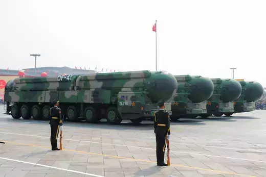 Two Chinese soldiers stand in front of four military vehicles carrying DF-41 intercontinental ballistic missiles.