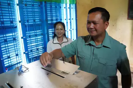 Cambodian politician Hun Manet wears a light green, short-sleeve shirt while placing his paper ballot in a box.