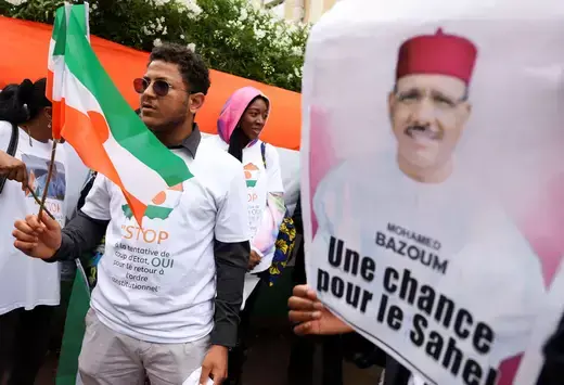 A demonstrator holds the Niger flag while another holds a poster that reads "Mohamed Bazoum: Une chance pour le Sahel." 