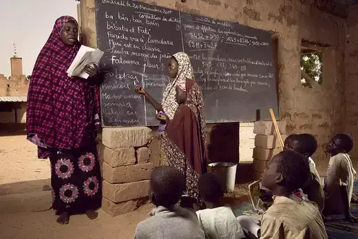 A woman reads in front of a chalkboard in an outdoor classroom in Niger.