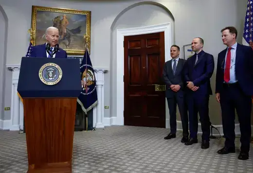 President Joe Biden as seen standing at a podium with the POTUS seal.