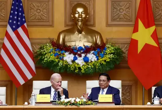 U.S. President sits a table next to Vietnam's prime minister with national flags and a bust of Ho Chi Minh placed behind them.