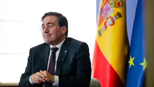 José Manuel Albares sitting next to Spanish flag