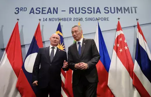 Russian President Vladimir Putin and Singaporean Prime Minister Lee Hsien Loong stand next to each other in front of the flags of ASEAN countries.