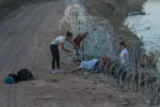 A woman from Colombia helps her children crawl past concertina wire, deployed to deter migrants, after they crossed the Rio Grande river into Eagle Pass, Texas, U.S. July 27, 2023. 