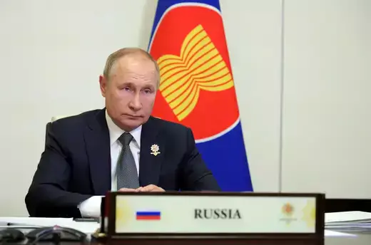 President Vladimir Putin sits at a desk with a flag behind him.