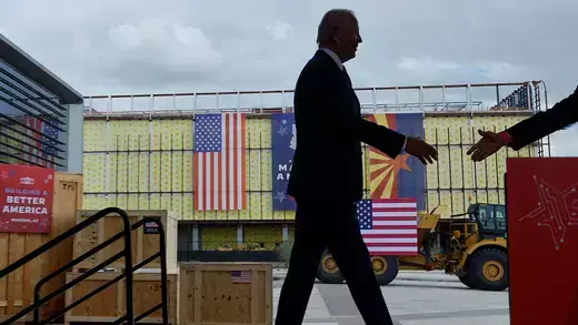 Joe Biden walking on stage about to shake hands at a Semiconductor Fabrication Plant in Arizona