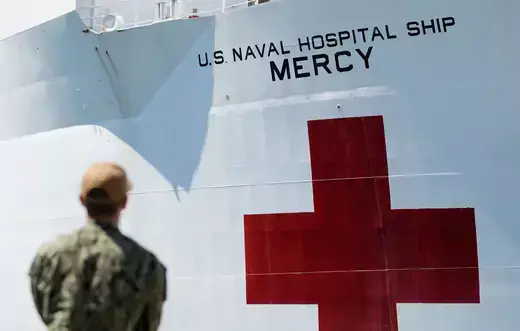 A soldier stares at a white U.S. Navy ship with a red cross.