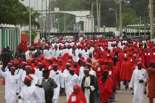 Hundreds of newlywed couples are seen wearing red and white clothes and walking in a large crowd.