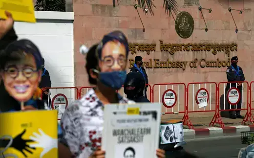 Protestors stand in front of a red brick wall of the Cambodian Embassy in Bangkok while holding paper posters of the face of the abducted Thai dissident, Wanchalearm Satsaksit.