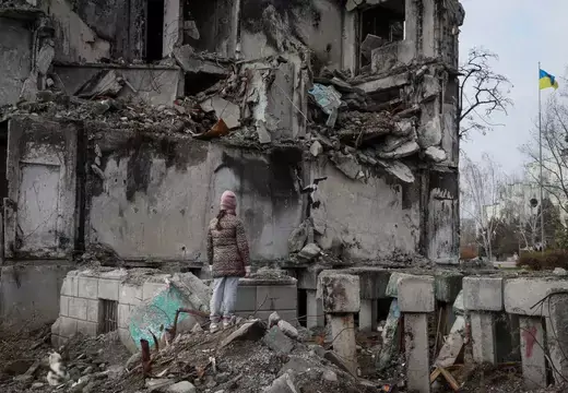 Ukrainian woman looks at rubble of destroyed building.
