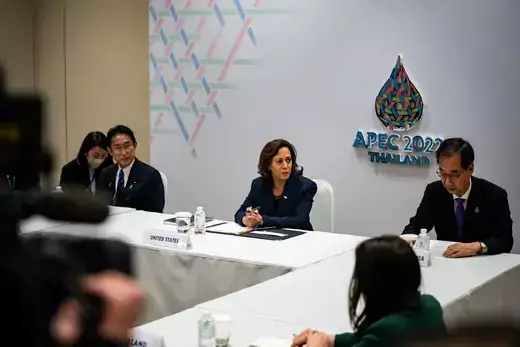 U.S. Vice President Kamala Harris wears a blue suit while sitting at a table with a white tablecloth and white background, while other leaders also wear blue suits.