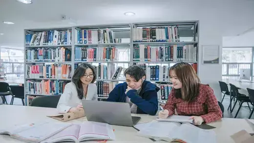 A group of three students studying together in a university library.