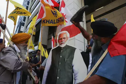 Protestors hold wooden signs and stand in front of a cardboard cutout of Indian Prime Minister Narendra Modi.