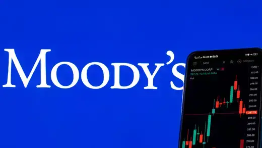 A photo illustration of a phone displaying stock market information of Moodys Investors Services with the company logo in the background.