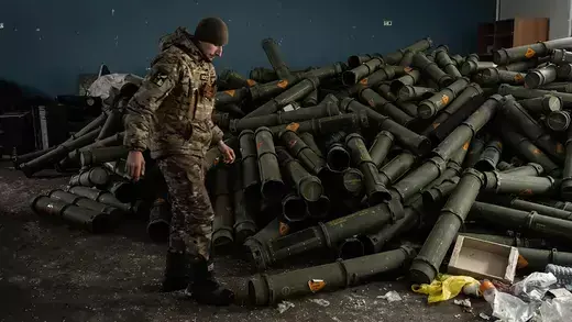 A Ukrainian soldier looks down at a pile of empty mortar shell containers.