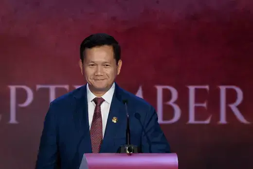Cambodian Prime Minister Hun Manet stands at a purple podium wearing a blue suit and maroon tie while standing in front of a maroon background.