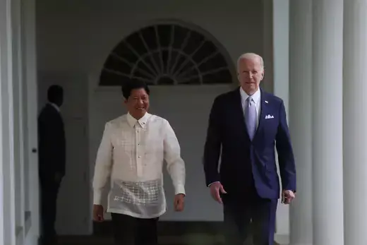 Philippine President Marcos wears a white button-down shirt while he walks past white colonnades with U.S. President Biden, who wears a blue suit.