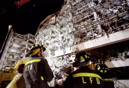 Two firefighters as viewed looking at the wreckage of a federal building.