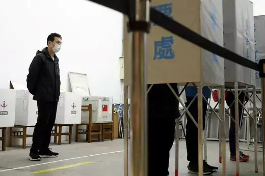 An electoral worker as viewed watching a row of voters at a polling station.
