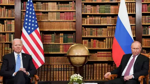 U.S. President Joe Biden and Russian President Vladimir Putin seated in front of a display of books, with the flags of both nations in the background.