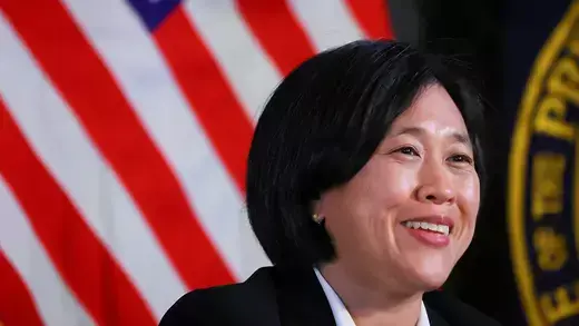 Katherine Tai is smiling with an American flag in the background.