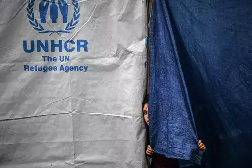 A child peeks out from a blue and white tent managed by the UN refugee agency.